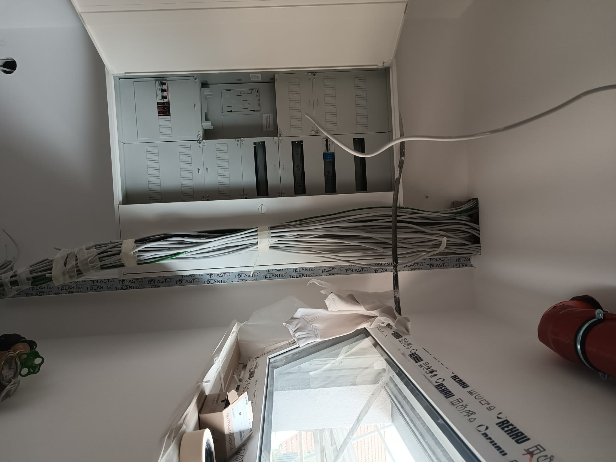 Otwarta rozdzielnica elektryczna z rzędami aparatów i opisanymi polami obwodów pompy ciepła i fotowoltaiki, z wiązką przewodów wprowadzoną od góry.